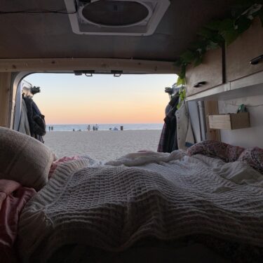 Inside a van looking onto a sandy beach and ocean at sunset