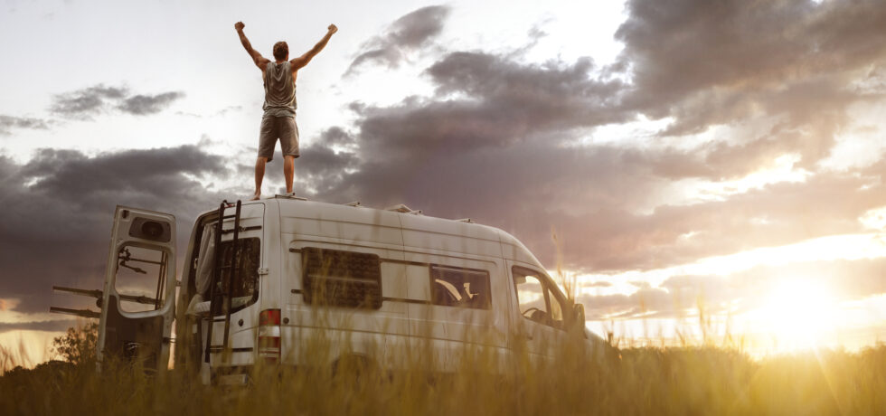Man with raised arms on top of his camper van - living in a camper van