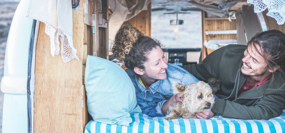 smiling couple laying in back of van conversion with dog