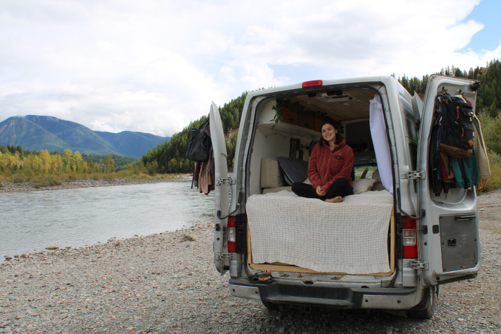 A girl sits in the back of her van with the back doors open near Glacier National Park.