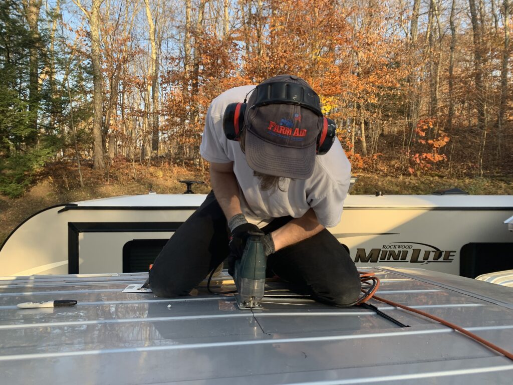A man uses a jigsaw to cut the roof of his van in order to install a van roof fan.