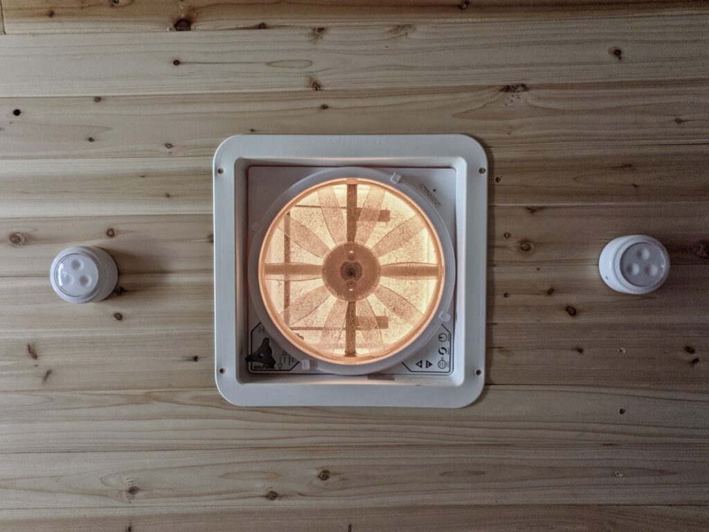 A van roof fan installed among a cedar plank ceiling.