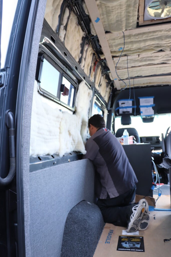 Man installing insulation and weatherproofing to a camper van interior