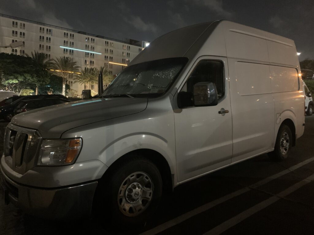 A Nissan NV 2500 stealth camping in a hotel parking lot.
