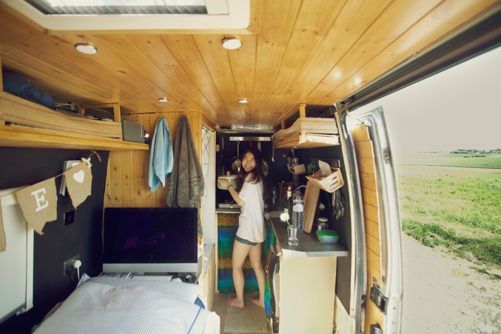 Woman cooking inside her camper van with the door open to a green pasture - living in a camper van