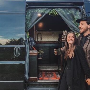 Young couple standing outside camper van with cat in the background