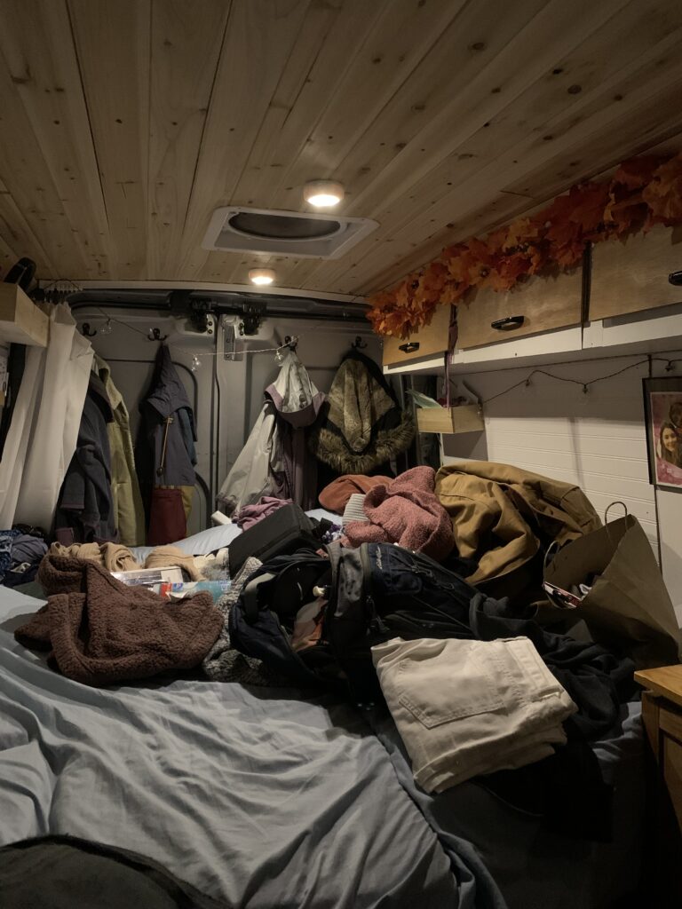 The interior of a camper van bed covered with clothing and other items.
