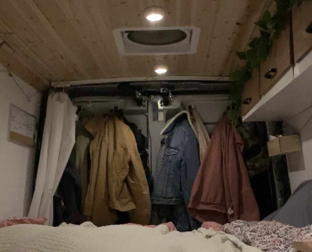 The interior of a camper van with coats hanging on hooks on the back doors.