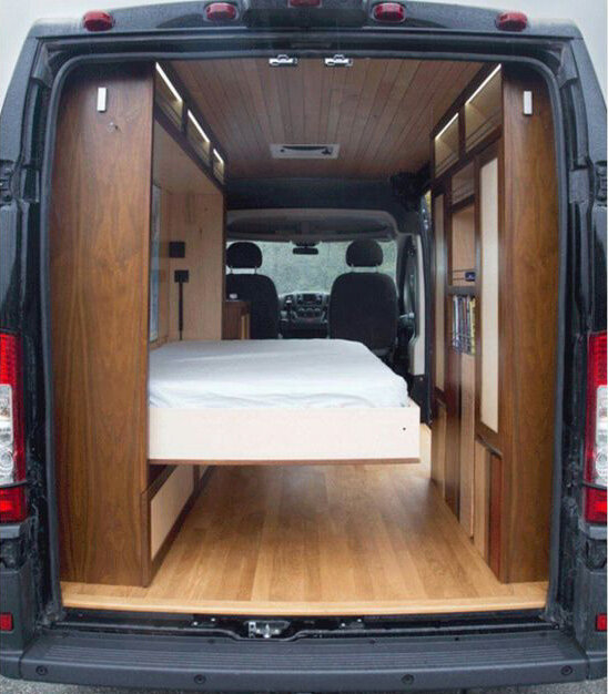 Interior of a camper van with wood designs. A murphy bed is laid out from the left side wall.