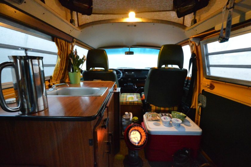 The interior of a camper van with a portable propane heater on and placed in the center of the van.
