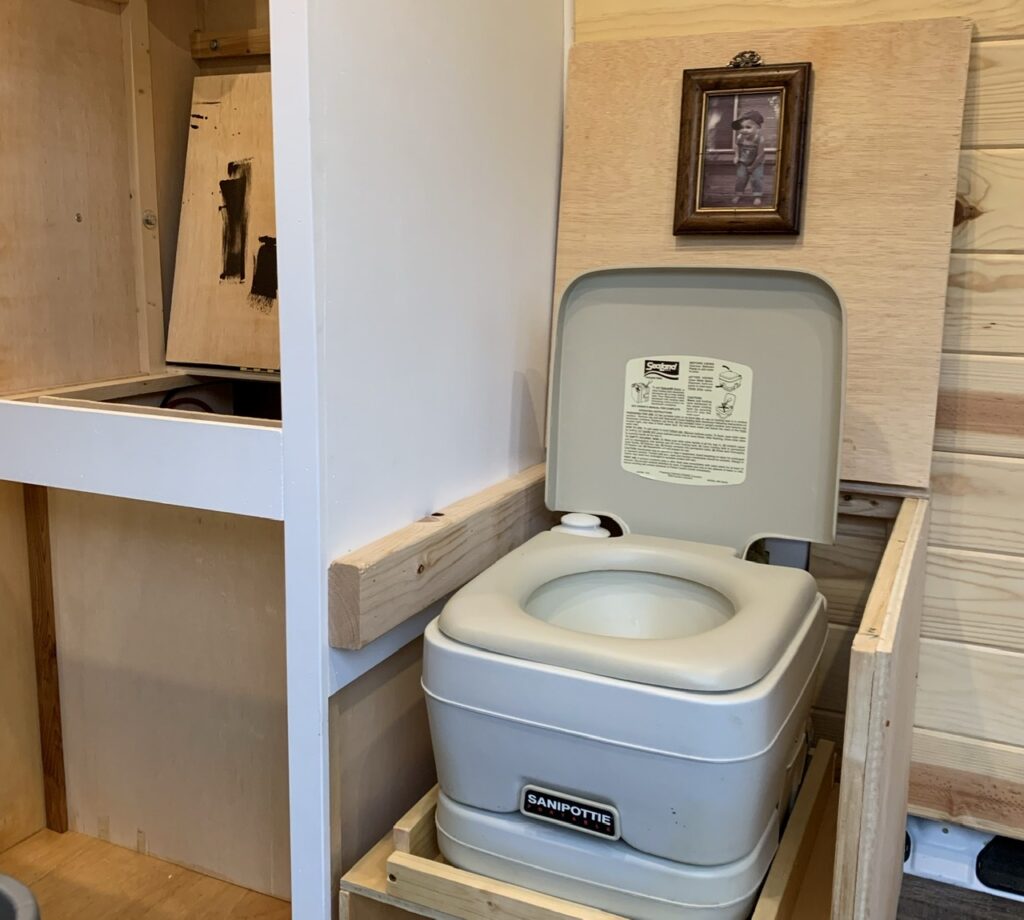 A cassette toilet sitting in its own compartment within a camper van.