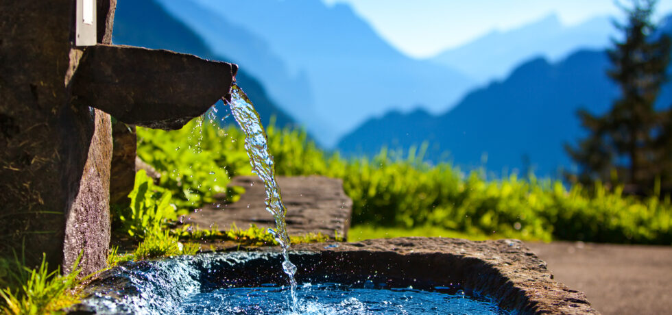 Clear water pouring out of a fountain with mountains in the background.
