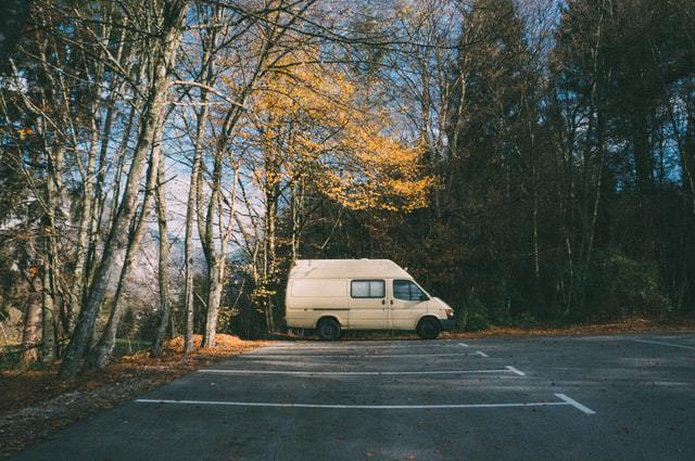 Off white camper van parked in a parking lot surrounded by woods