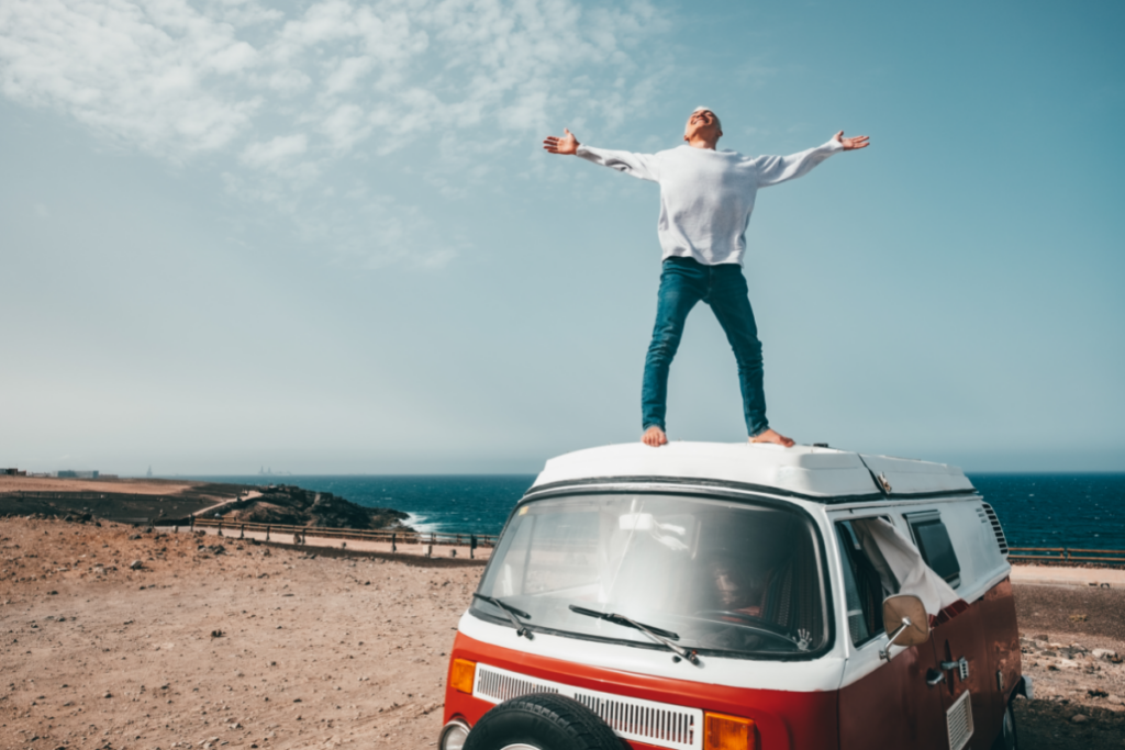 A man standing on top of a VW Westfalia van on the beach