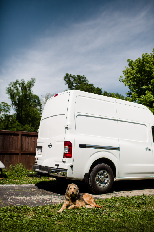  A camper van sitting in a driveway, with a dog sat in front of it. 