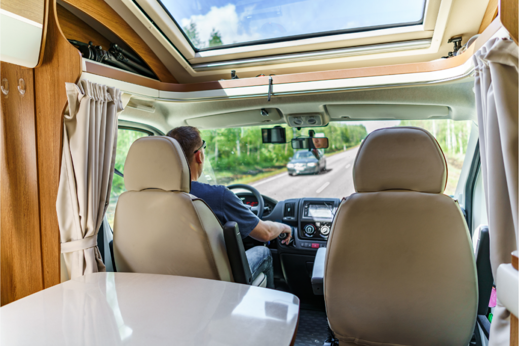 A man driving a van, seen from behind in the interior of a camper van