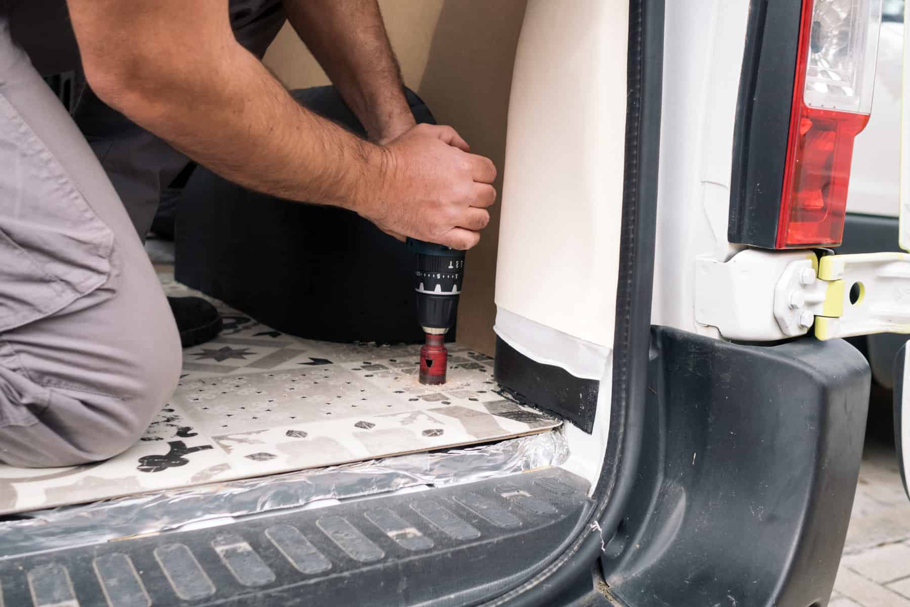 Guy drilling hole through floor of a van - van build mistakes