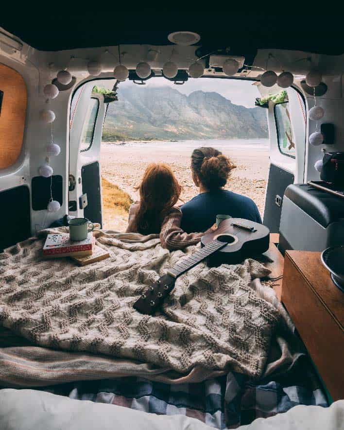 Two people sitting outside a van conversion while camping.