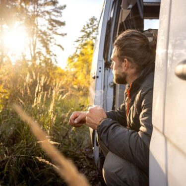 Man enjoying a morning coffee in the doorway of his camper van