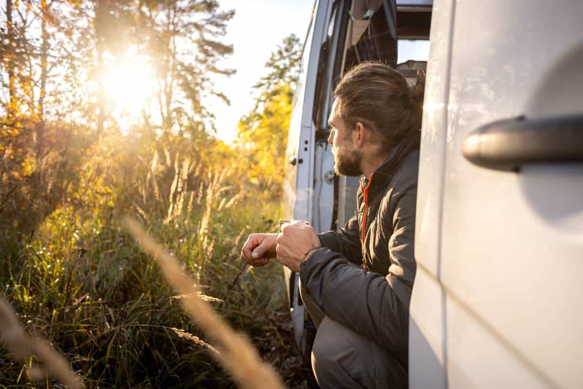 Man enjoying a morning coffee in the doorway of his camper van
