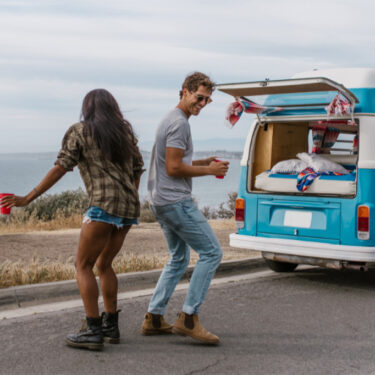 A man and a woman dancing outside of their camper van after a long road trip