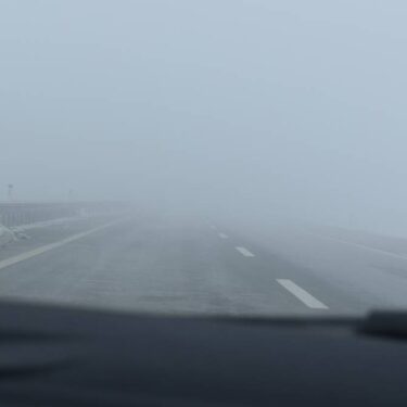 Windshield view of driving in fog down a highway