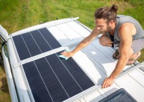 man demonstrating how to clean RV solar panels on the roof of a camper van