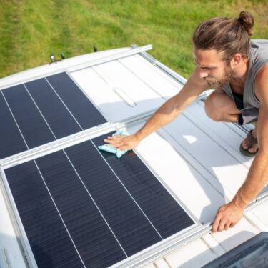 man demonstrating how to clean RV solar panels on the roof of a camper van
