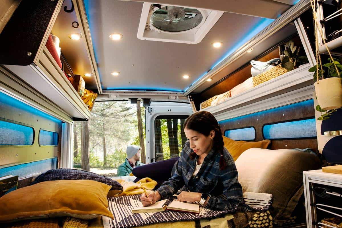 a woman writing in a notebook on the bed inside a converted Ford Transit Trail van