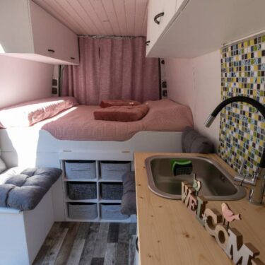 interior of a camper van conversion featuring kitchen countertop with sink, bench, and bed
