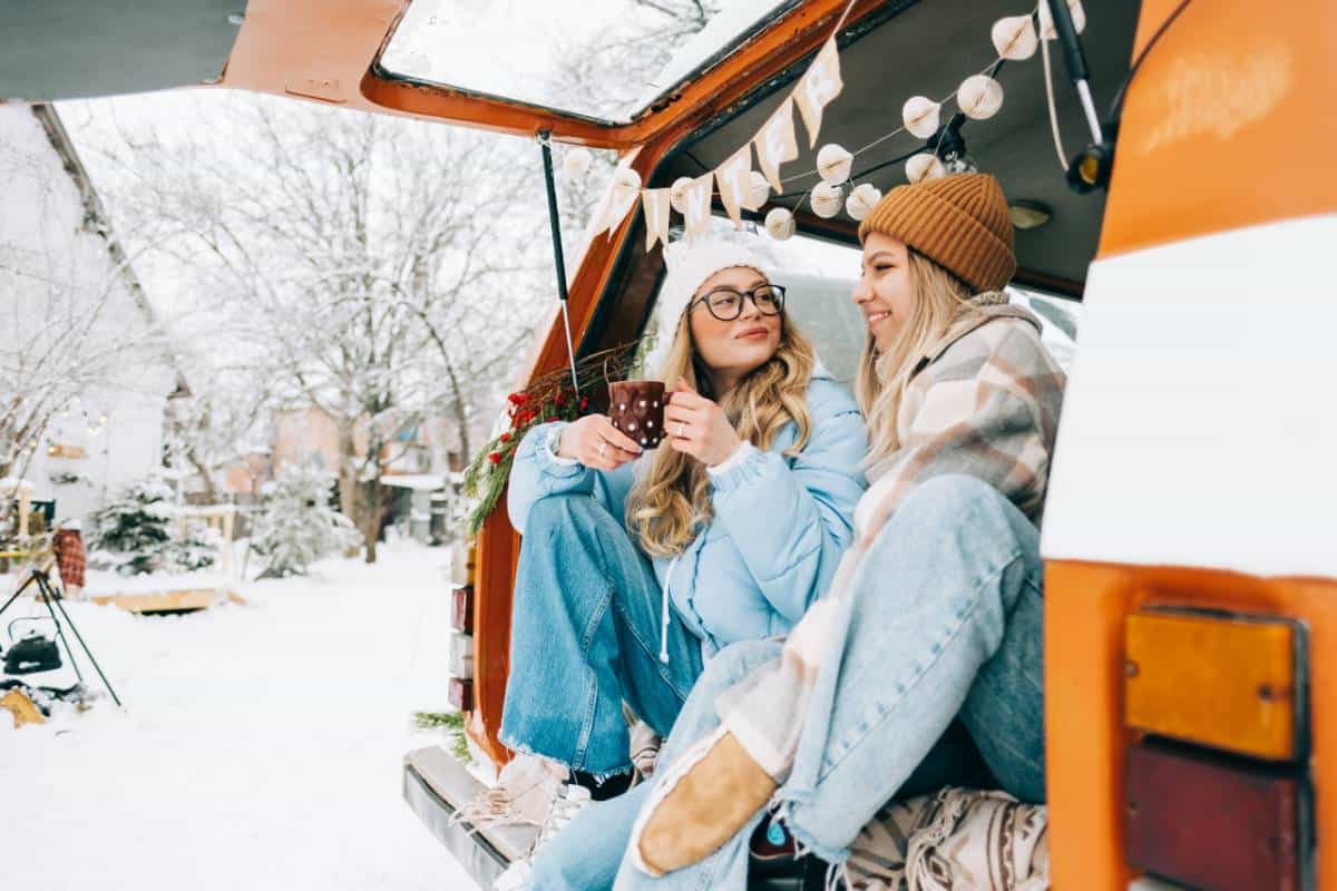 Two cheerful women friends sitting in a van at a campground in winter surrounded by snow