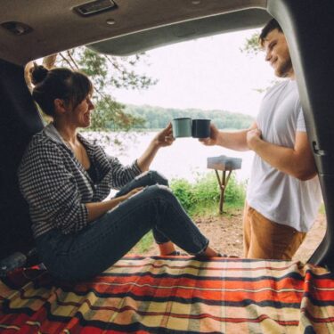 couple drinking coffee and relaxing from the back of an SUV while car camping