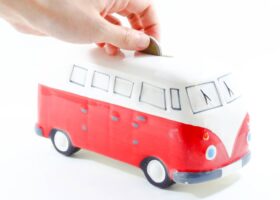 hand putting coin in a Volkswagen van piggy bank