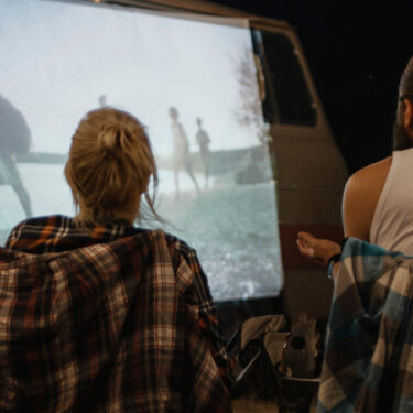 Campers watching a movie projected onto a van