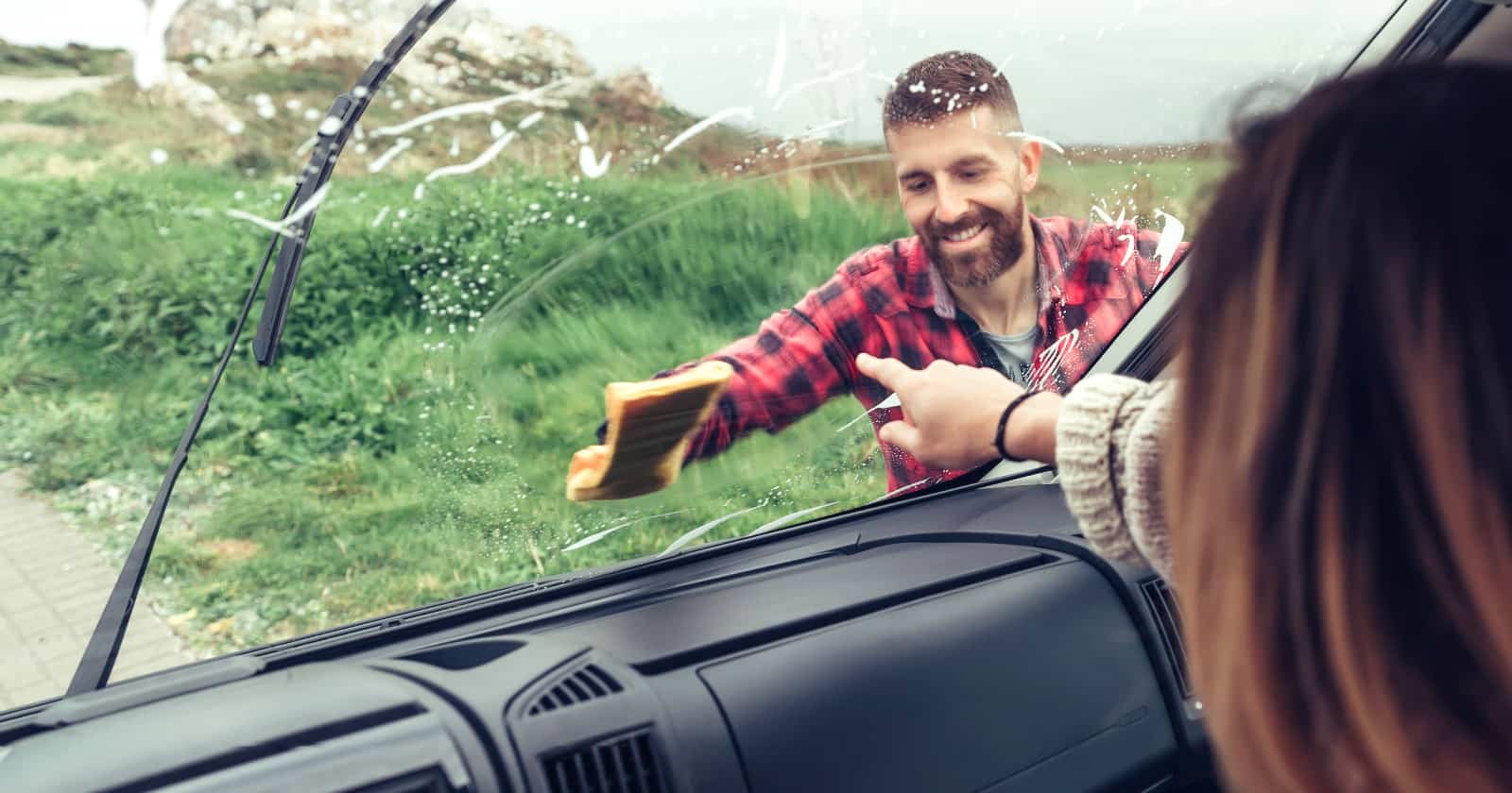 Man smiling spring cleaning van windshield with cloth while woman pointing stain