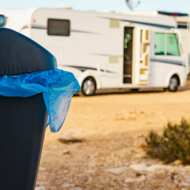camping trash bag with plastic bag inside it, mounted to the inside of a campervan door and overlooking a small motorhome parked by water