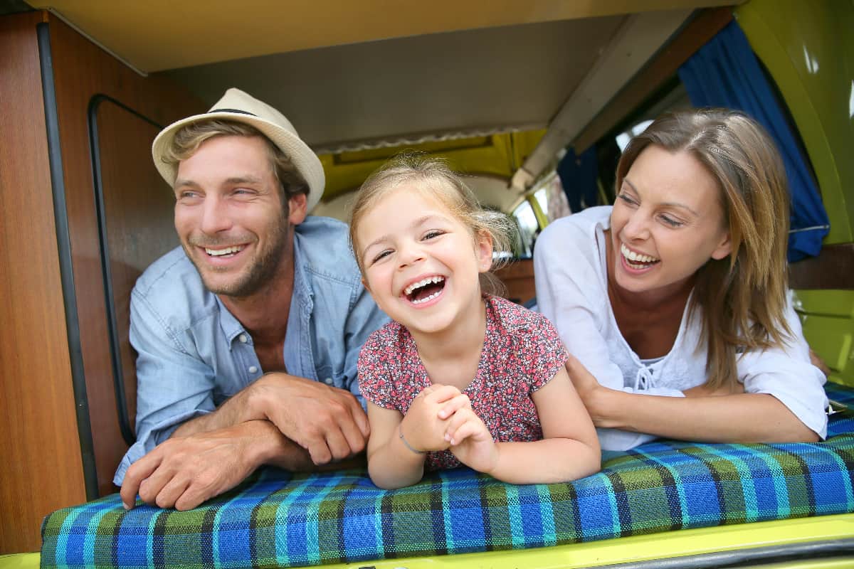 Caucasian Dad, Mom, and young daughter smiling  at camera while laying on a mattress in a family-friendly van design