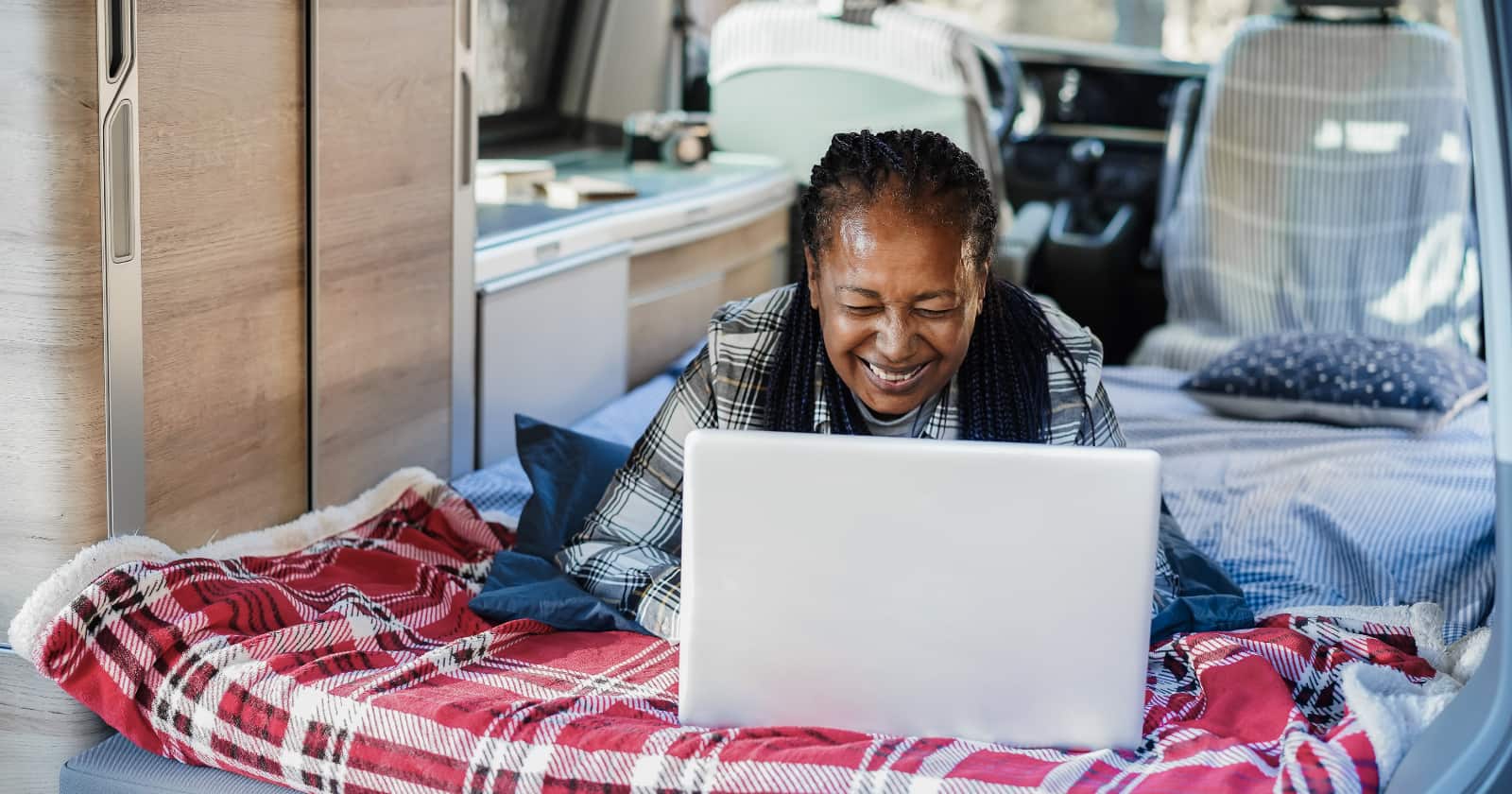 Solo senior camper woman having fun inside camper van using laptop computer on her bed