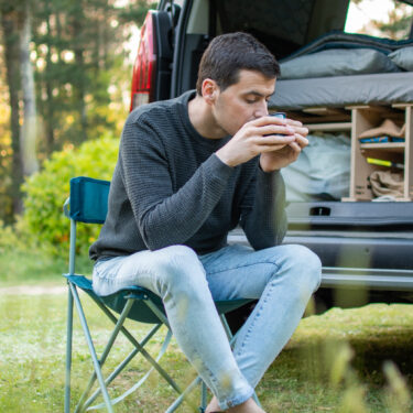 Young man drinking coffee next to his camper van.