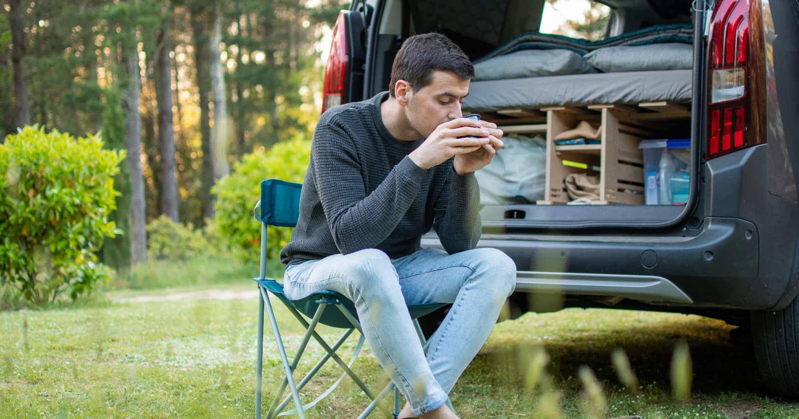 Young man drinking coffee next to his camper van.