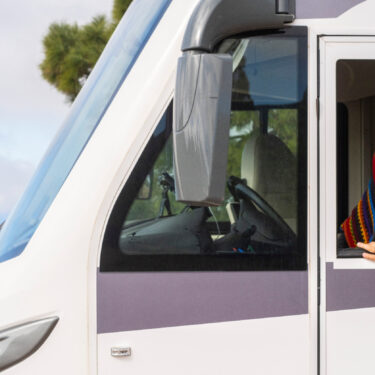 woman driver outside the window of her camper van looking forward to traveling to bucket list destinations