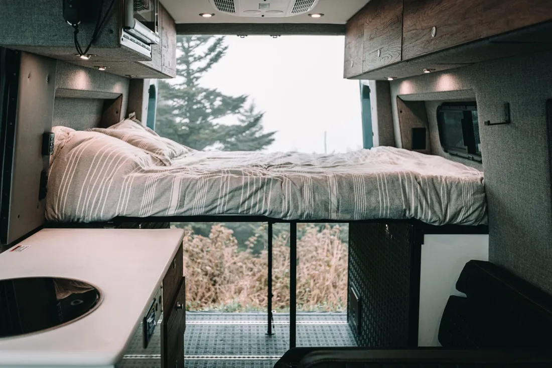 Bed and sink shown amidst open back door of a camper van.