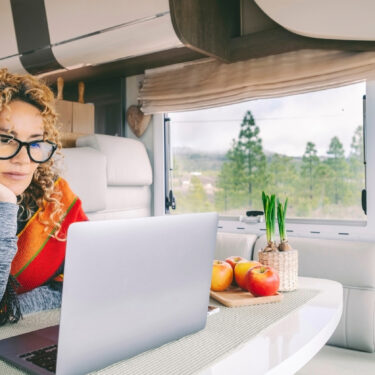 Independent woman sitting inside a camper van in smart remote working job activity using laptop.