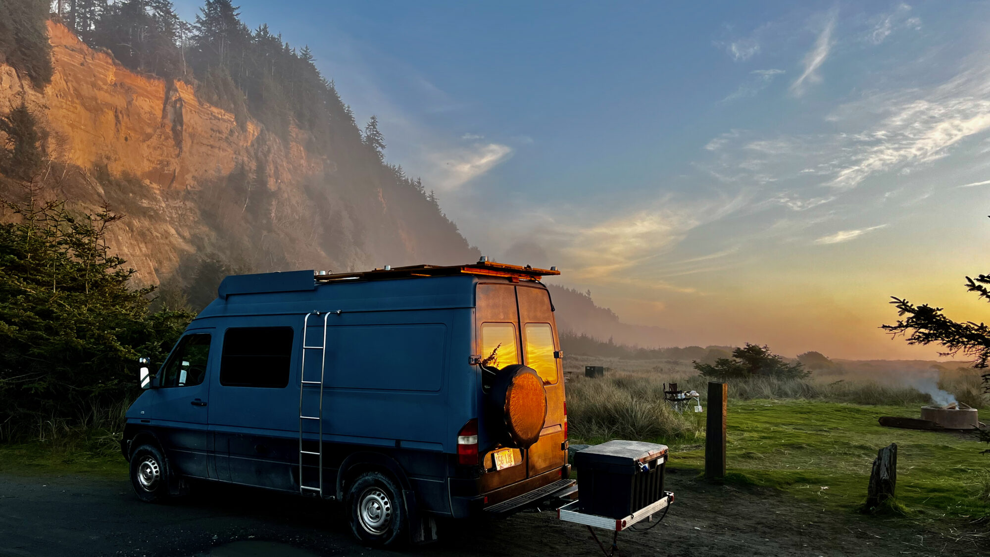 van is parked on a scenic overlook, with the sun casting a warm glow on a cliffside in the background. 