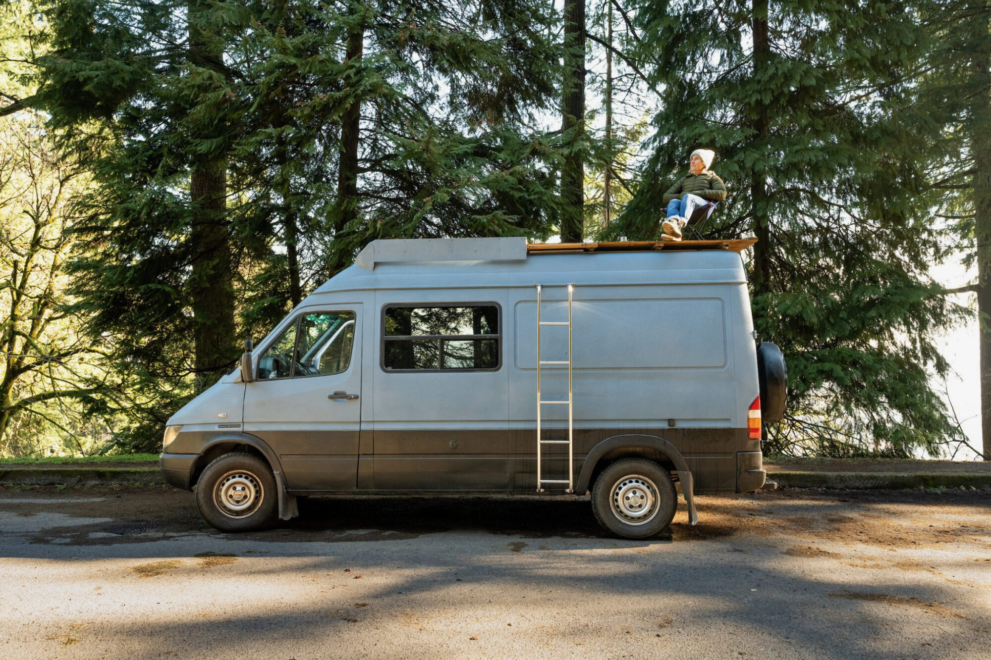 A serene outdoor scene where a person is lounging on top of a vintage white van.